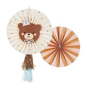 Pode incluir: Dois leques decorativos de papel. Um é creme com bolinhas douradas e um rosto de urso marrom usando um chapéu de festa. O outro leque tem listras alternadas de pêssego e bege. Ambos os leques são redondos e adequados para uma festa.