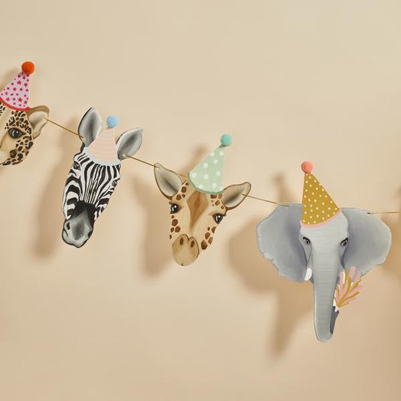 May include: A whimsical animal-themed party banner featuring a zebra, giraffe, elephant, and leopard, each adorned with a festive party hat. The banner is strung on a thin gold string, perfect for a children's birthday party or safari-themed event.