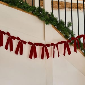 May include: A decorative garland featuring a series of deep red velvet bows strung together in a horizontal line. Each bow has two long, hanging tails and is spaced evenly along a thin cord, creating a festive and uniform appearance for display.