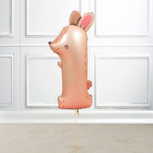 Pode incluir: Um grande balão de folha de ouro em forma de número um com um rosto de rato de desenho animado. O rato tem orelhas cor-de-rosa, olhos castanhos e um pequeno nariz cor-de-rosa.