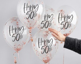 Puede incluir: Cinco globos transparentes llenos de confeti oro rosa. Cada globo tiene la inscripción "Happy 50th" en escritura negra. Los globos están atados con cintas de oro rosa.