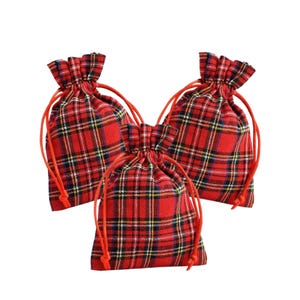 May include: Three red plaid drawstring bags with orange drawstrings. The bags feature a classic tartan pattern in red, black, yellow, and white. The bags are made of fabric and are gathered at the top.