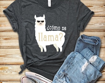 Puede incluir: Una camiseta gris oscura con una llama blanca que lleva gafas de sol y el texto "¿cómo se llama?" impreso en la parte delantera.