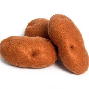 May include: Three brown felt potatoes are arranged on a white background. The potatoes have a textured surface and a slightly elongated shape, with small indentations. The felt material gives them a soft, handcrafted appearance.