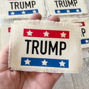 May include: A white fabric patch with frayed edges featuring the word "TRUMP" in black letters and three red stars and three blue stars.