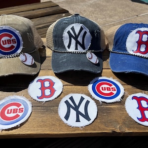 May include: Three baseball caps with team logos: Chicago Cubs, New York Yankees, and Boston Red Sox. Each cap has a distressed look with a mesh back and a baseball charm. Additional team logo patches are also displayed.