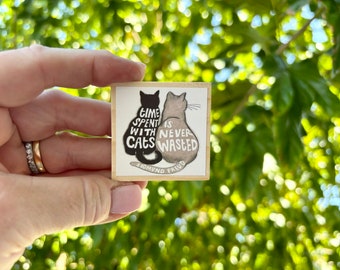 May include: A wooden block with a black and white illustration of two cats. The text reads "Time spent with cats is never wasted - Sigmund Freud".