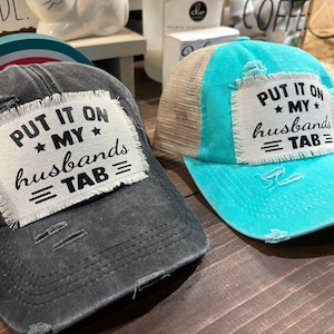 May include: Two trucker hats with distressed fabric and a white patch that reads "PUT IT ON MY HUSBANDS = TAB =" in black text.