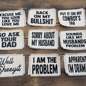 May include: Nine rectangular patches with frayed edges, each displaying a different humorous phrase in black text. Phrases include "Excuse Me, You Look Like You Love Me" and "I Am The Problem."