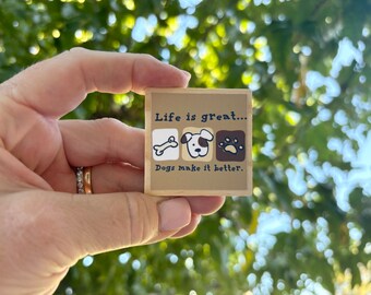 May include: A wooden block with the text "Life is great... Dogs make it better."  The block has a brown background with white and black illustrations of a bone, a dog's head, and a paw print.