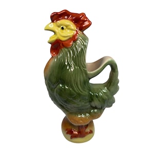 May include: A ceramic rooster pitcher with a green body, yellow beak, and red comb and wattle. The pitcher has a handle and is perched on a yellow and brown base. The rooster is a decorative kitchenware item.