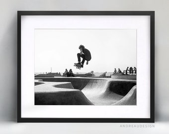 May include: Black and white photograph of a skateboarder performing a trick in a skate park. The skateboarder is in mid-air, with their board facing the camera. The skate park is in the background, with ramps and other obstacles.