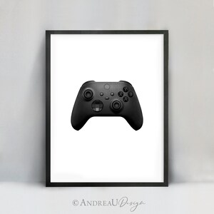 May include: A black video game controller with buttons labeled A, B, X, Y, and a directional pad. The controller is framed in a black picture frame.