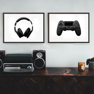 May include: Two framed prints on a white wall, one with a black pair of headphones and the other with a black video game controller. A wooden shelf with a stereo system, a record, a candle, and a potted plant sits below the prints.
