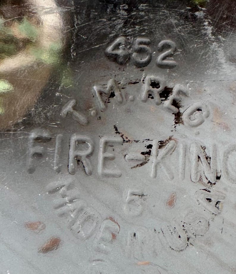 May include: Close-up of a gray, distressed metal surface with the embossed text "452", "T.M. REG", and "FIRE KING". The text "MADE IN USA" and the number "5" are also visible. The surface has scratches and wear.