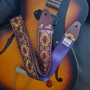 May include: Purple and gold guitar strap with a brown leather end and a label that reads "PatB.o.  Hand Crafted".
