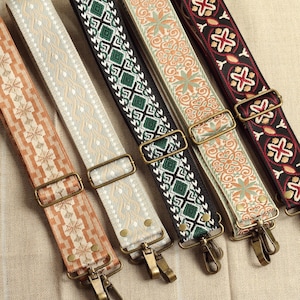 Peut inclure: Cinq bandoulières réglables présentant des motifs tissés distincts en orange, crème, noir et vert, et beige. Chaque sangle comprend des curseurs en métal couleur laiton antique et des mousquetons pivotants pour la fixation aux sacs.