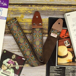 Puede incluir: Una correa de guitarra de cuero marrón con un diseño estampado de colores. La correa tiene un extremo de cuero marrón con el texto "Pardo Guitar Straps".