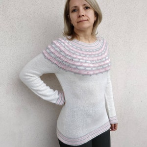 Puede incluir: Suéter de punto blanco con un yugo estampado en rosa y gris. El suéter tiene un corte holgado y mangas largas.