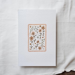 May include: A white card with a pink border around a watercolor illustration of a floral pattern. The flowers are orange and brown with green stems and leaves.