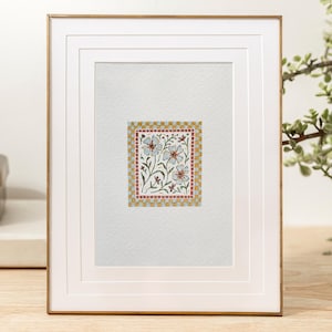 K&ouml;nnte beinhalten: Ein gerahmtes Aquarellbild mit einem floralen Design mit wei&szlig;en Bl&uuml;ten und gr&uuml;nen Bl&auml;ttern. Die Blumen sind von einem roten und goldenen Musterrahmen umgeben.