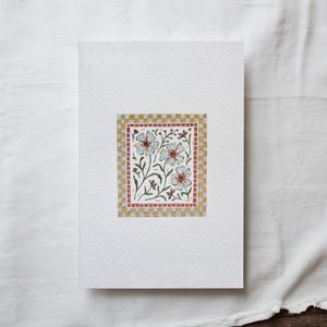 K&ouml;nnte beinhalten: Eine wei&szlig;e Karte mit einem floralen Design, das von einem gelben und roten karierten Rahmen umgeben ist. Die Blumen sind blau und wei&szlig; mit gr&uuml;nen Stielen und Bl&auml;ttern.