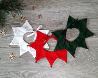May include: Three star-shaped pet collars in white, red, and green with gold bells around the edges. The collars have a ribbon tie closure.