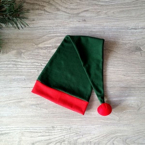 May include: A green elf hat with a red trim and a red pom-pom on the end.