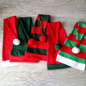Può includere: Quattro cappelli da elfo di Natale in rosso e verde con bordino bianco. I cappelli hanno motivi a strisce e pompon bianchi in cima.