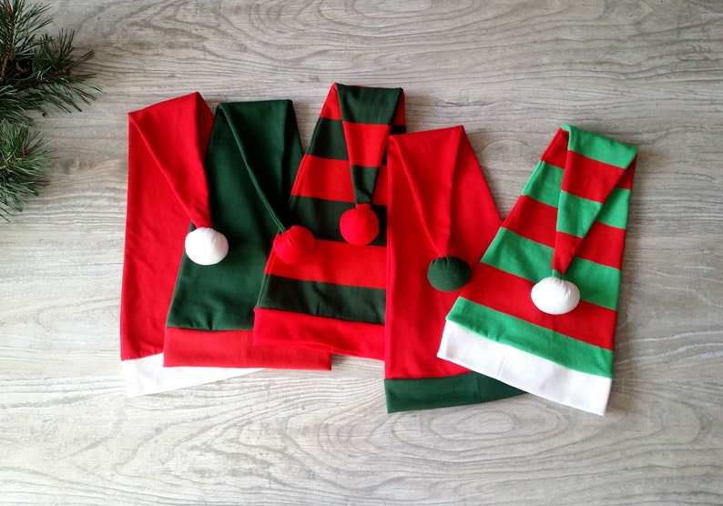 May include: Four Christmas elf hats in red and green with white trim. The hats have striped patterns and white pom-poms on top.