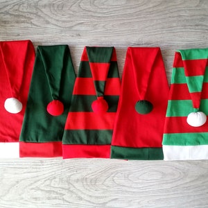 May include: Five Christmas elf hats in different designs. Two are red with green stripes, one is solid green, one is solid red, and one is green with red stripes. All have white pom-poms on top.