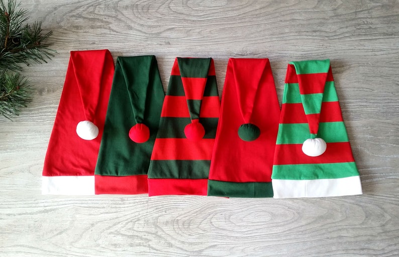 May include: Five Christmas elf hats in different designs. Two are red with green stripes, one is solid green, one is solid red, and one is green with red stripes. All have white pom-poms on top.