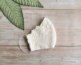 May include: White face mask with delicate lace trim. The mask is made of a soft, white fabric and has a simple design.