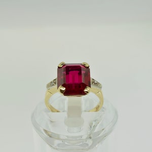 May include: A gold ring with a large, emerald-cut ruby gemstone and smaller diamond accents.