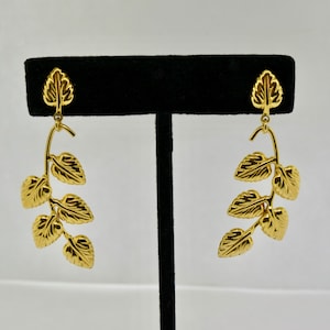 May include: A pair of gold leaf dangle earrings. Each earring features a curved stem with five leaves.