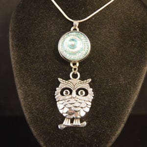 May include: A silver necklace with a blue and silver owl pendant. The owl has a round, blue, sparkly eye.