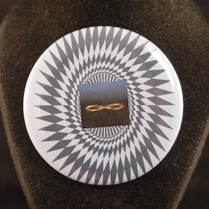 May include: A round, white button with a black and white spiral design. In the center of the spiral is a blue square with a gold infinity symbol.