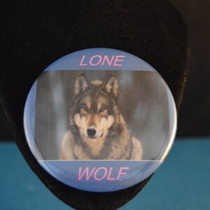 May include: A blue and white button with a picture of a wolf and the text "LONE WOLF" in pink.