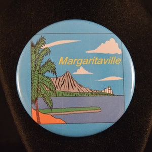 May include: A blue and white round button with a cartoon image of a palm tree, a mountain, and a building with the text "Margaritaville" in yellow.