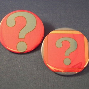 May include: Two round buttons with a question mark on each. The button on the left is red with a blue question mark. The button on the right is red with a blue question mark and a yellow, orange, and blue border.