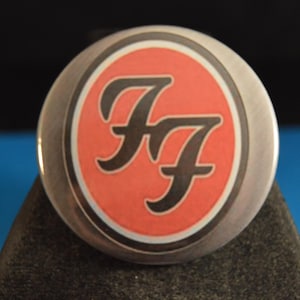 May include: A silver button with a red circle and the letters "FF" in black.