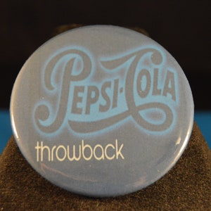 May include: A blue and white round button with the Pepsi-Cola logo and the text "throwback" in white.