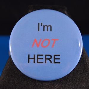 May include: A blue button with the text "I'm NOT HERE" in black and red lettering.