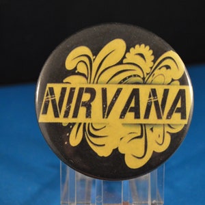 May include: A black and yellow button with the word "NIRVANA" in black letters on a yellow stripe. The background is a black and yellow floral design.