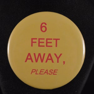 May include: A yellow round button with red text that reads "6 FEET AWAY, PLEASE".