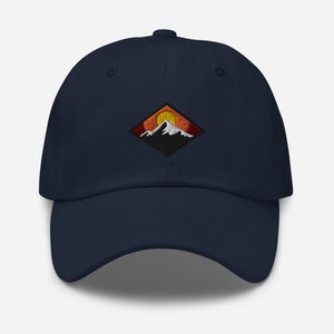 May include: A navy blue baseball cap with an embroidered patch featuring a mountain range with a setting sun. The patch is in a diamond shape with orange, yellow, and red colors.
