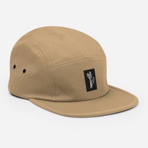 May include: A tan 5-panel cap with a black square patch featuring a white cactus illustration.