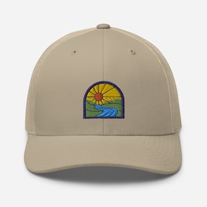 May include: A beige trucker hat with a patch featuring a stylized sun, river, and green hills. The patch is outlined in blue and has a yellow sun with orange rays.