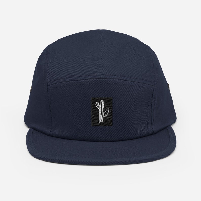 May include: A navy blue 5-panel cap with a black square patch featuring a white line drawing of a cactus.