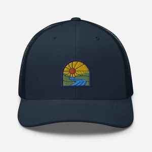 May include: A navy blue trucker hat with a patch of a sun setting over a river and hills. The patch has a yellow sun, blue river, green hills, and orange and purple accents.